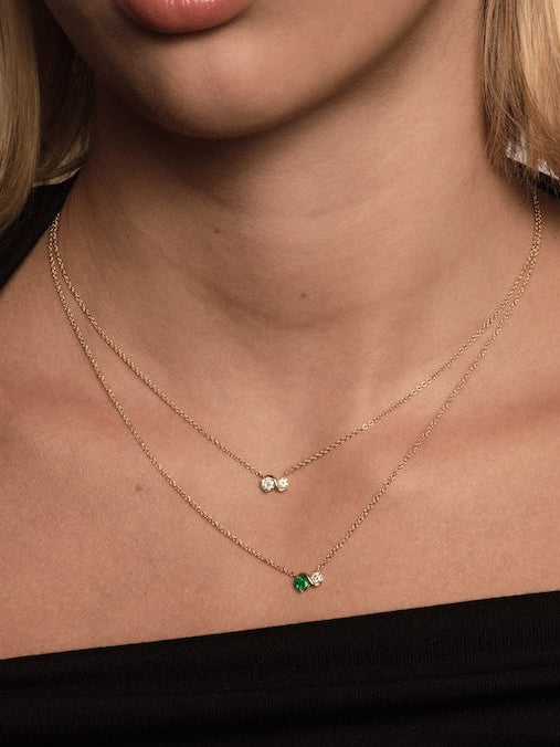 Close-up of a person wearing two gold necklaces with green and clear gemstones.