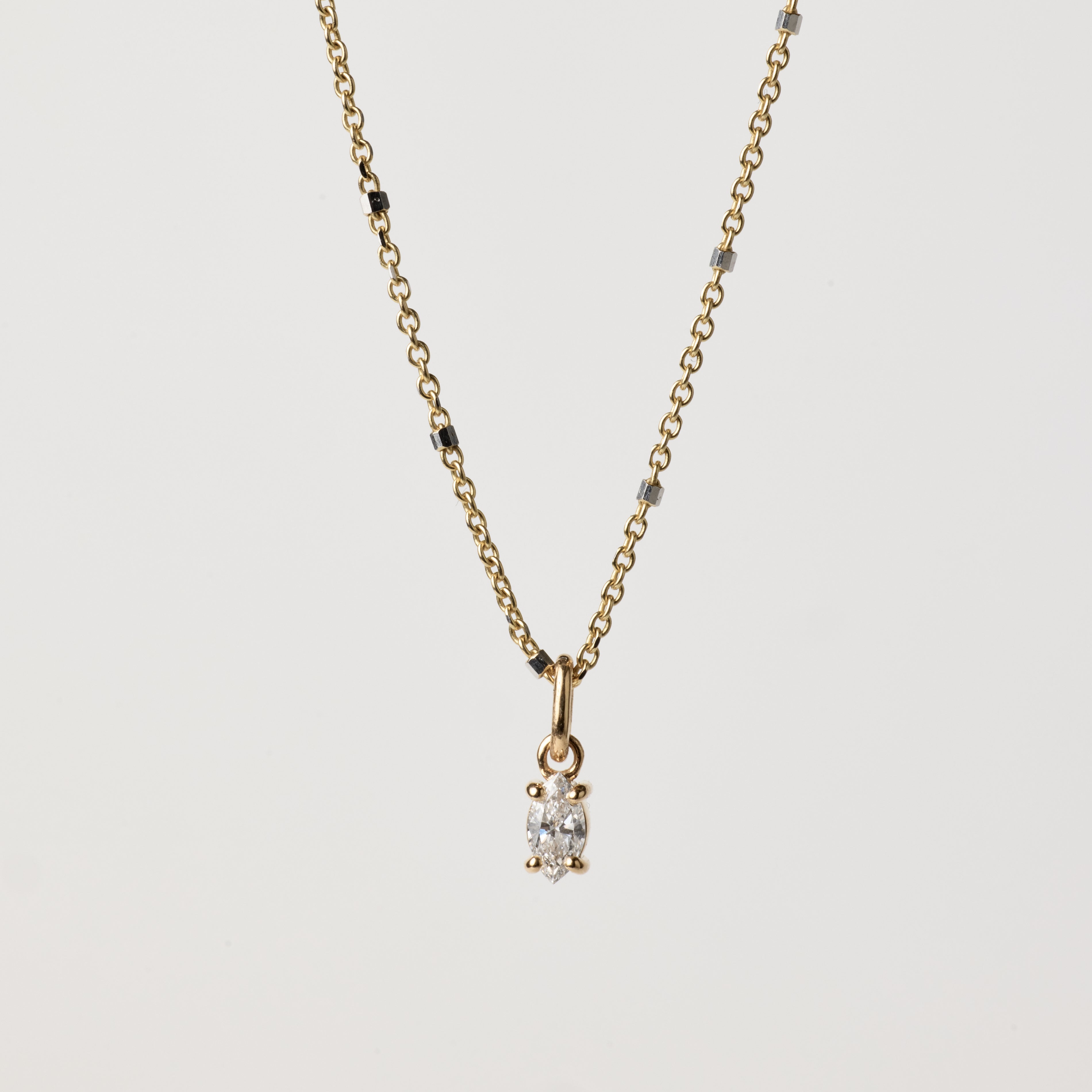 Gold necklace with a diamond pendant on a light gray background