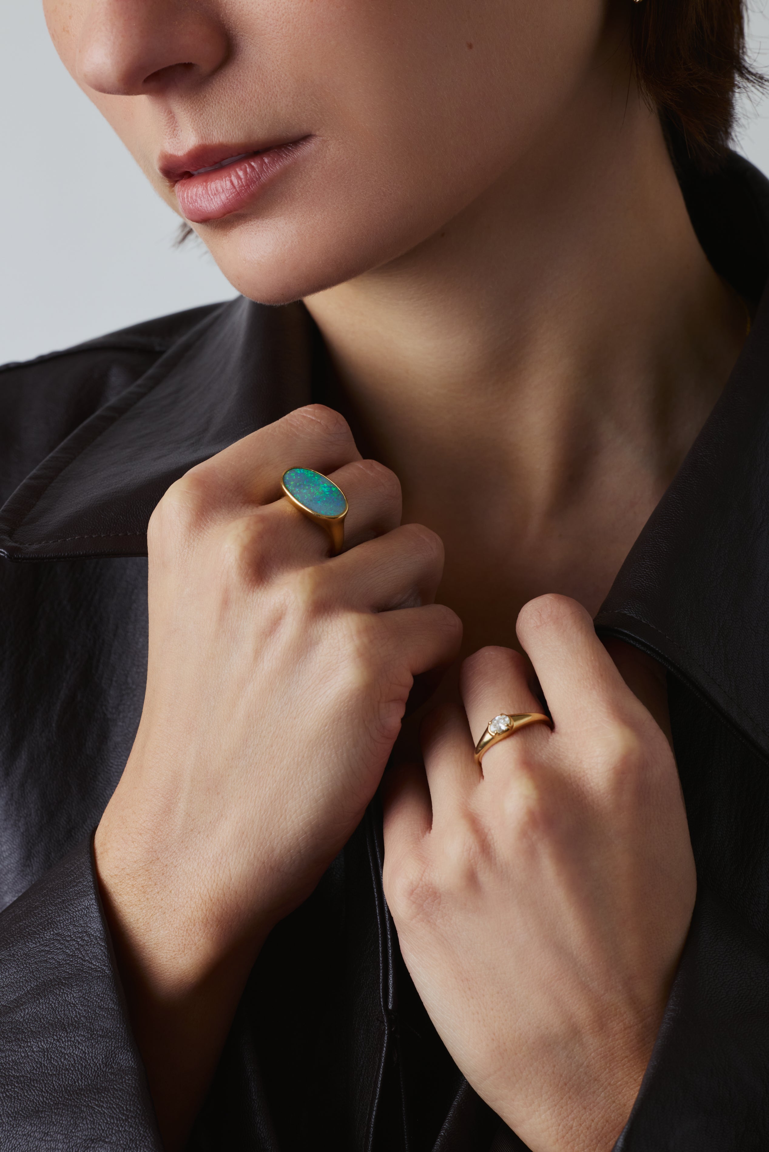Close-up of a person wearing two rings: a large oval turquoise ring on one finger and a slim gold band ring on the other, while wearing a black leather jacket.