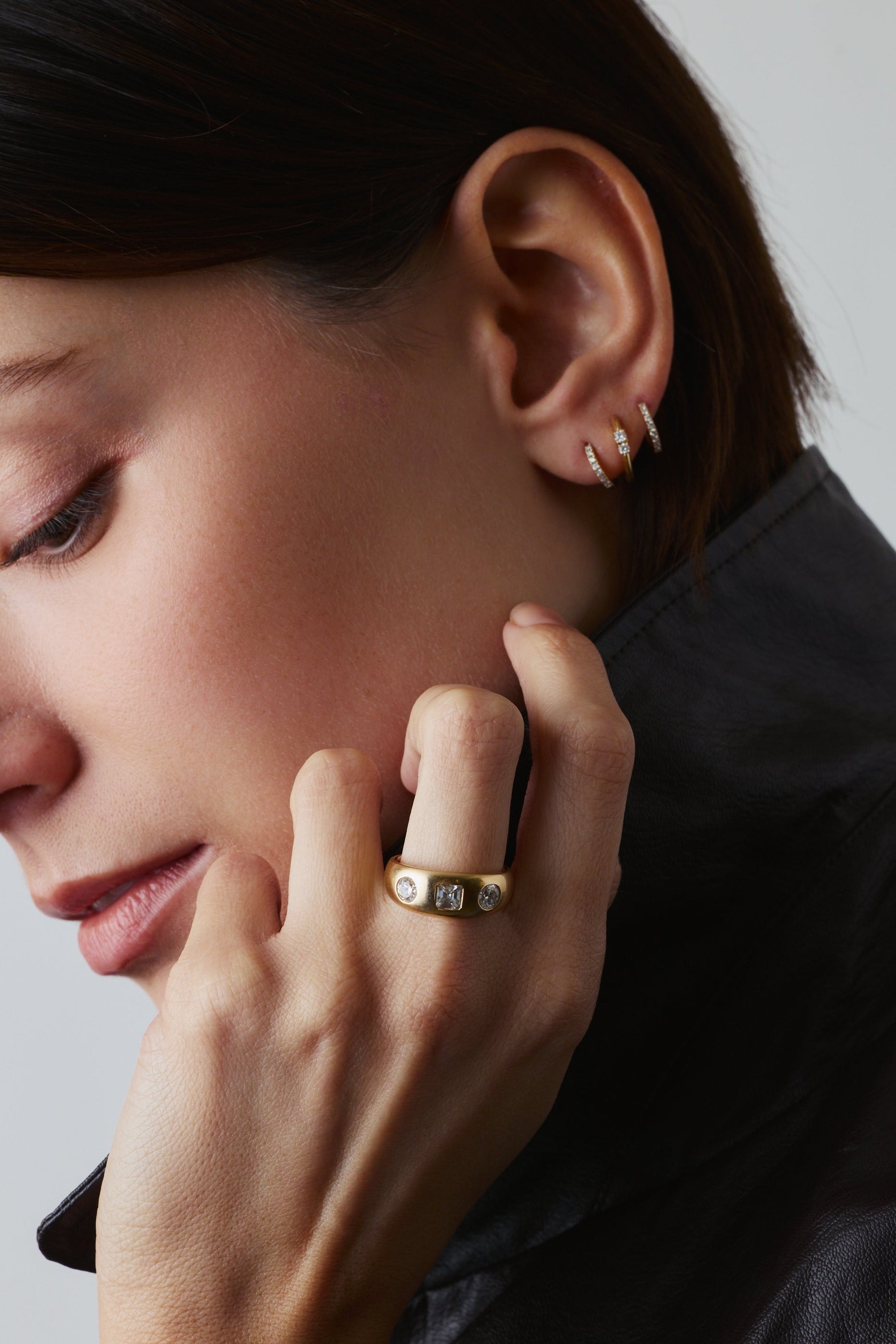 Close-up of a person wearing gold earrings and a ring, with a neutral background