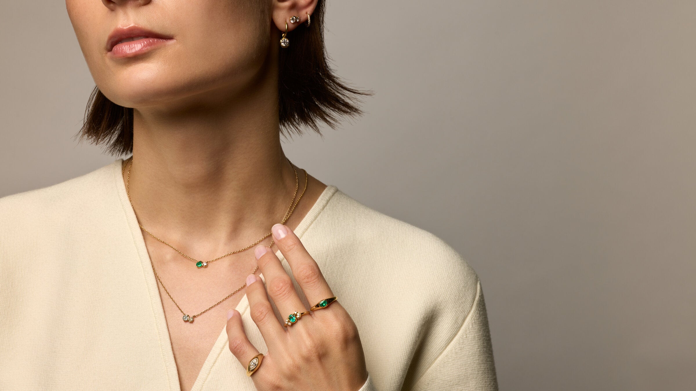 Model wearing gold necklaces, emerald and diamond rings and earrings in a cream knit